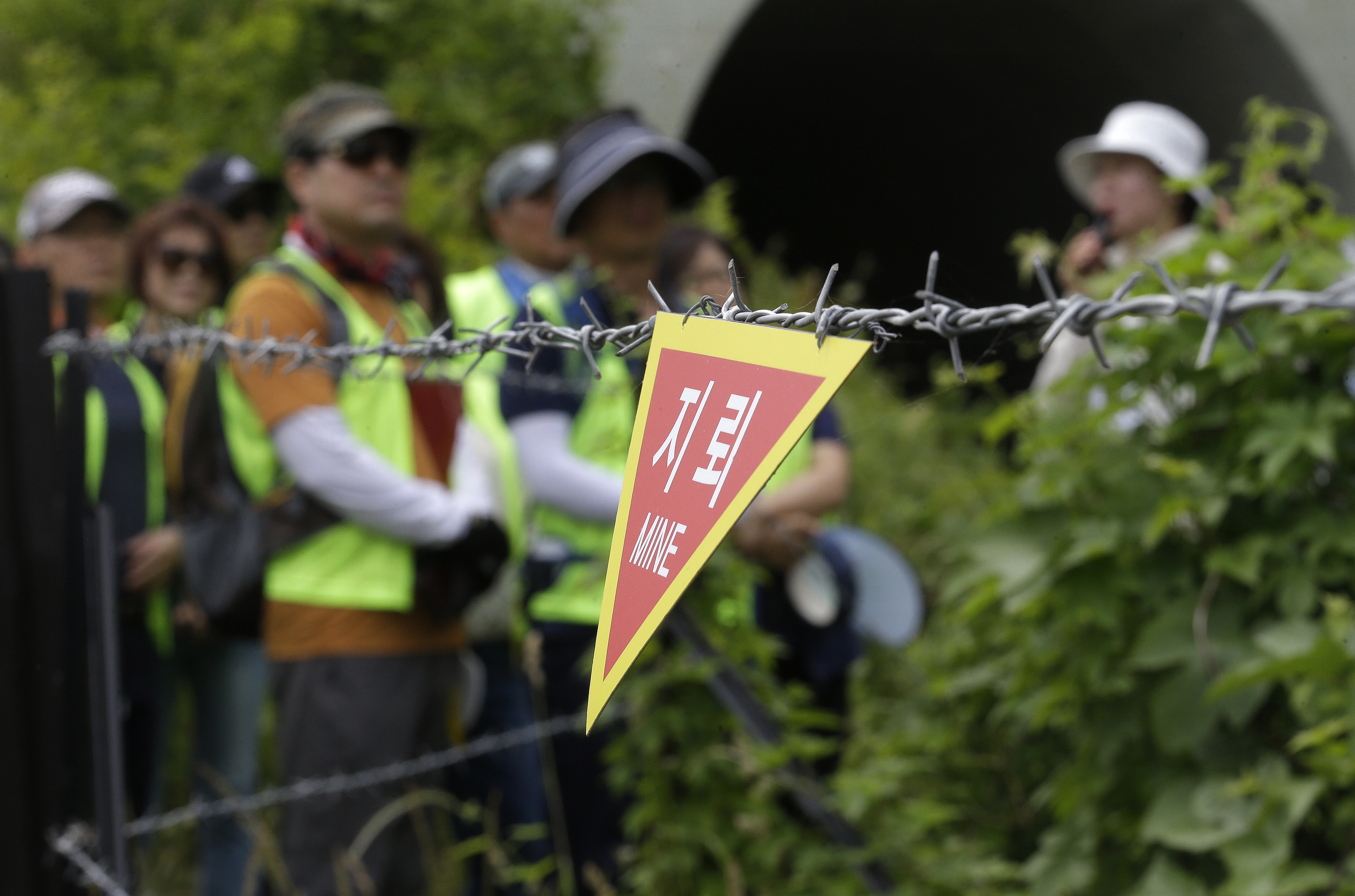 A sign indicating land mines is seen with people behind it.