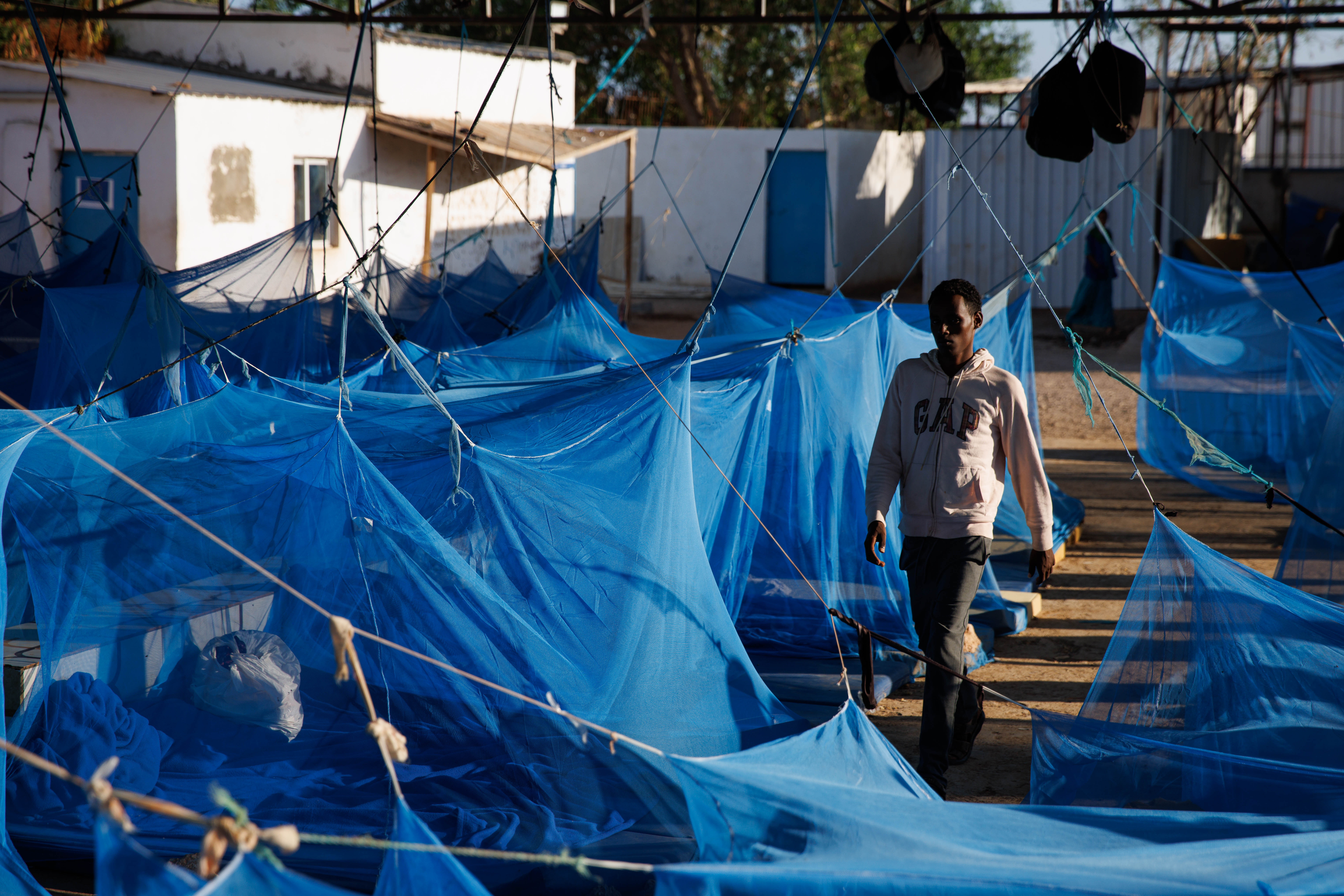 OBOCK, DJIBOUTI - JANUARY 18: A man walks through a male dormitory at an International Organization for Migration (IOM) transit centre for migrants returning from the Middle East on January 18, 2024 in Obock, Djibouti. The recent attacks on commercial ships by Yemen's Houthi rebel group, which have prompted a series of air strikes by the United States and its allies in response, have not just imperilled a vital shipping route, but also the popular "Eastern Route" for migrants heading from Ethiopia to Saudi Arabia, via Djibouti and the Bab al-Mandab Strait that connects the Gulf of Aden and Red Sea. The strait is also a heavily trafficked shipping route on the way to the Suez Canal. (Photo by Luke Dray/Getty Images)
