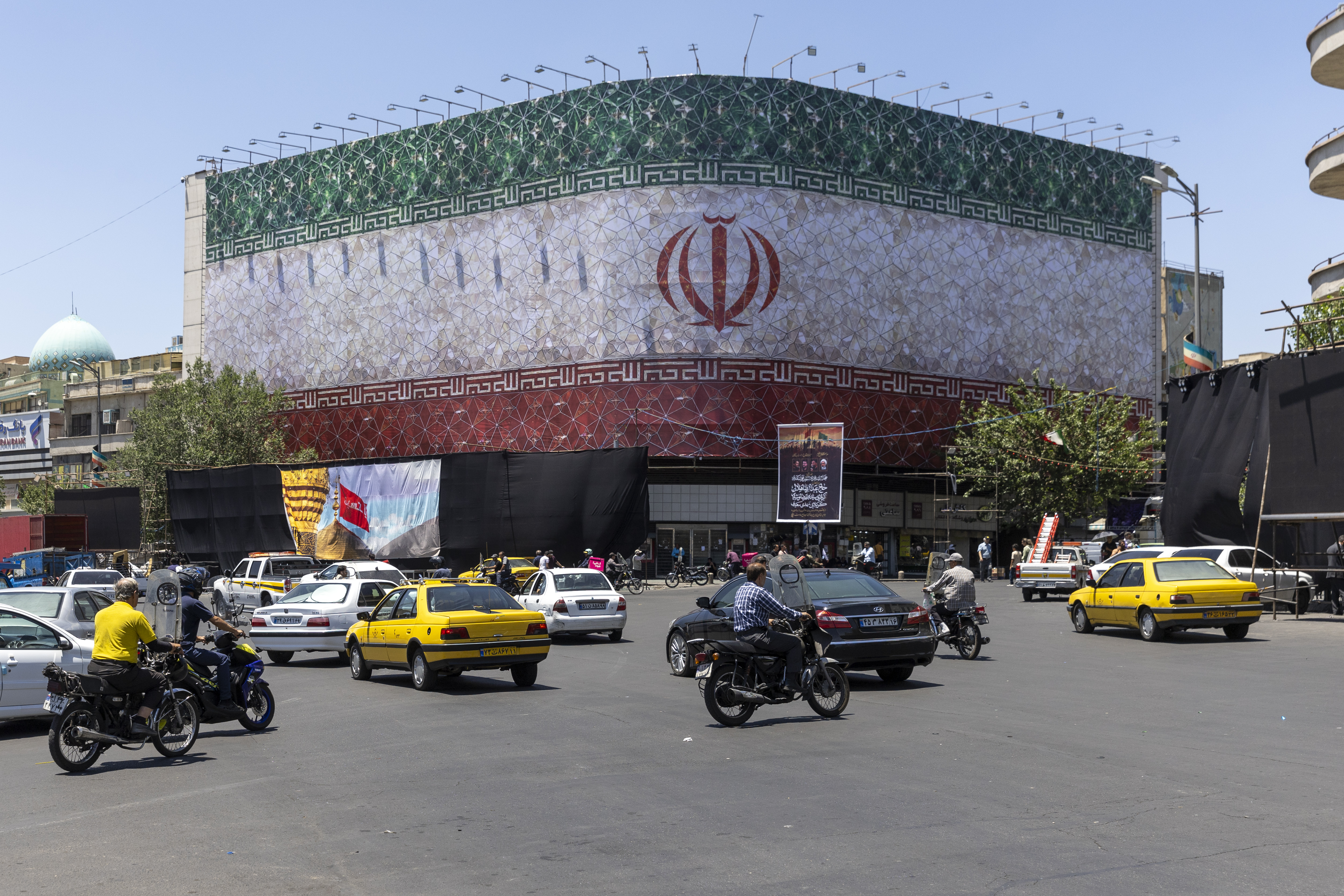 Cars and motorcycles are seen in front of a billboard displaying the Iranian flag