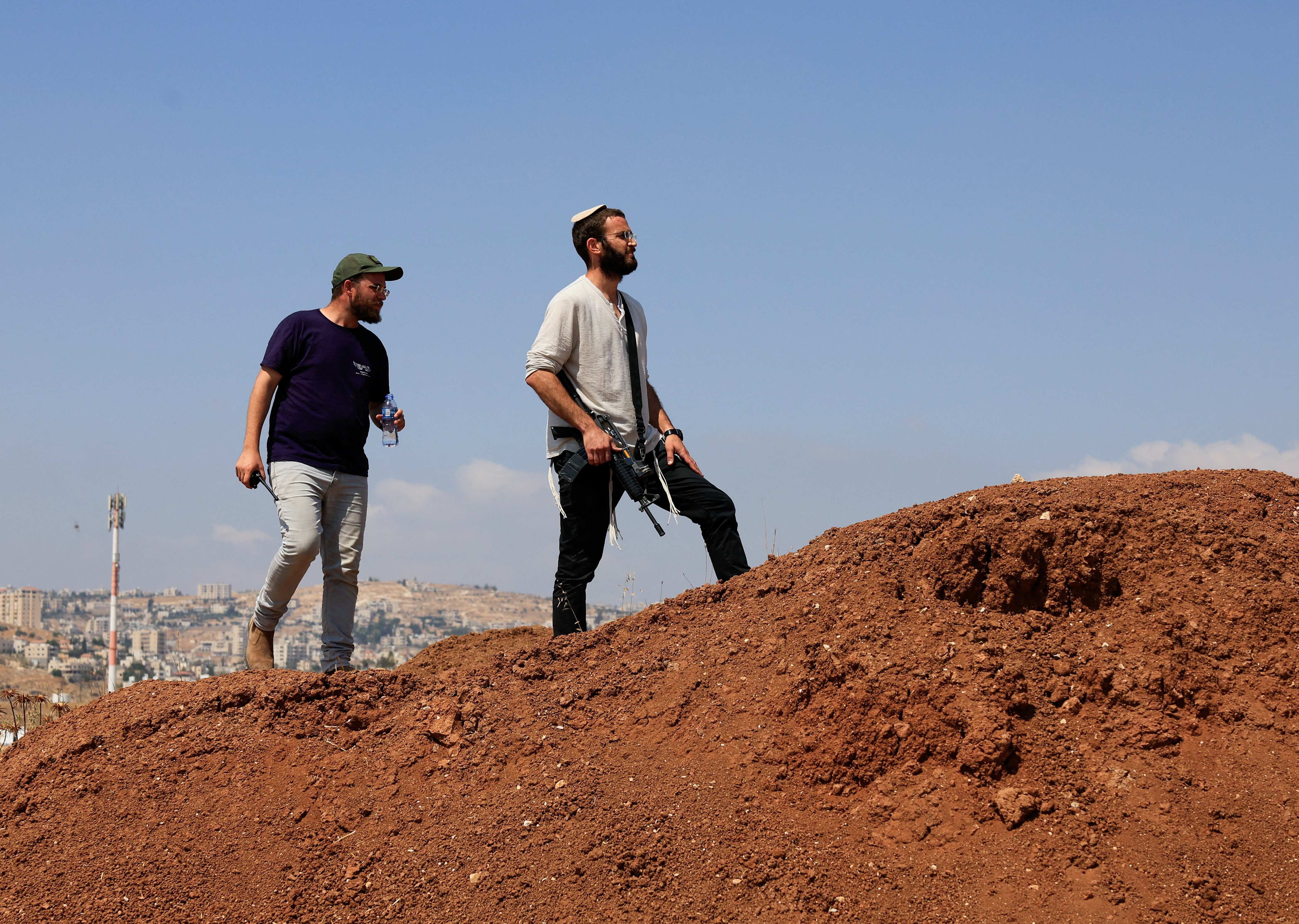 An armed Israeli settler looks on as Palestinian and Israeli activists accompany Palestinian landowners in their property, which is threatened with confiscation by Israeli settlers, in Beit Sahour in the Israeli-occupied West Bank August 14, 2026. REUTERS/Mussa Qawasma