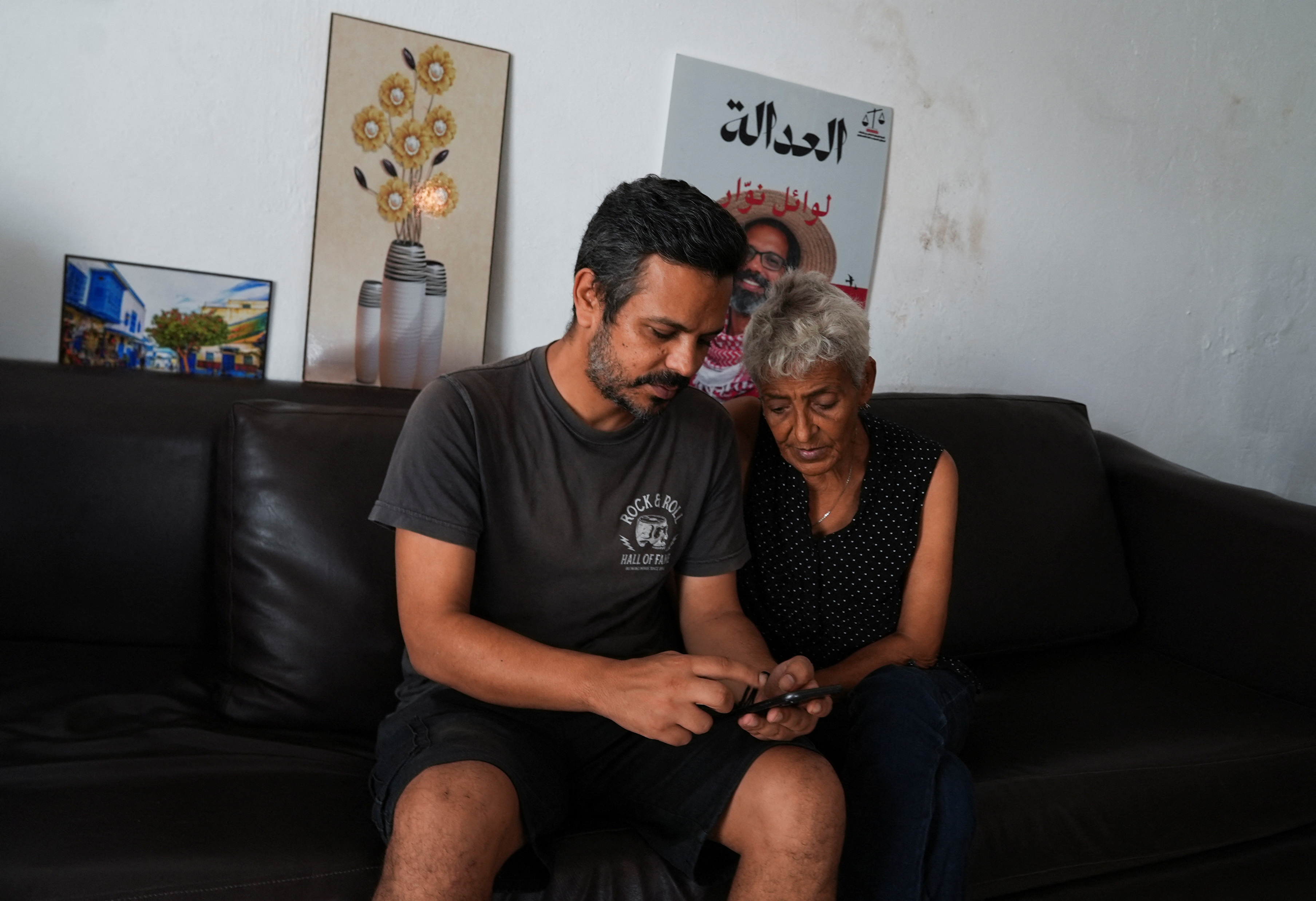 Hamida Dridi, mother of detained pro-Palestinian activist Wael Naouar, sits with her son, Nabil Naouar, as they look at a phone at their home in Tunis, Tunisia. [Stringer/Reuters]